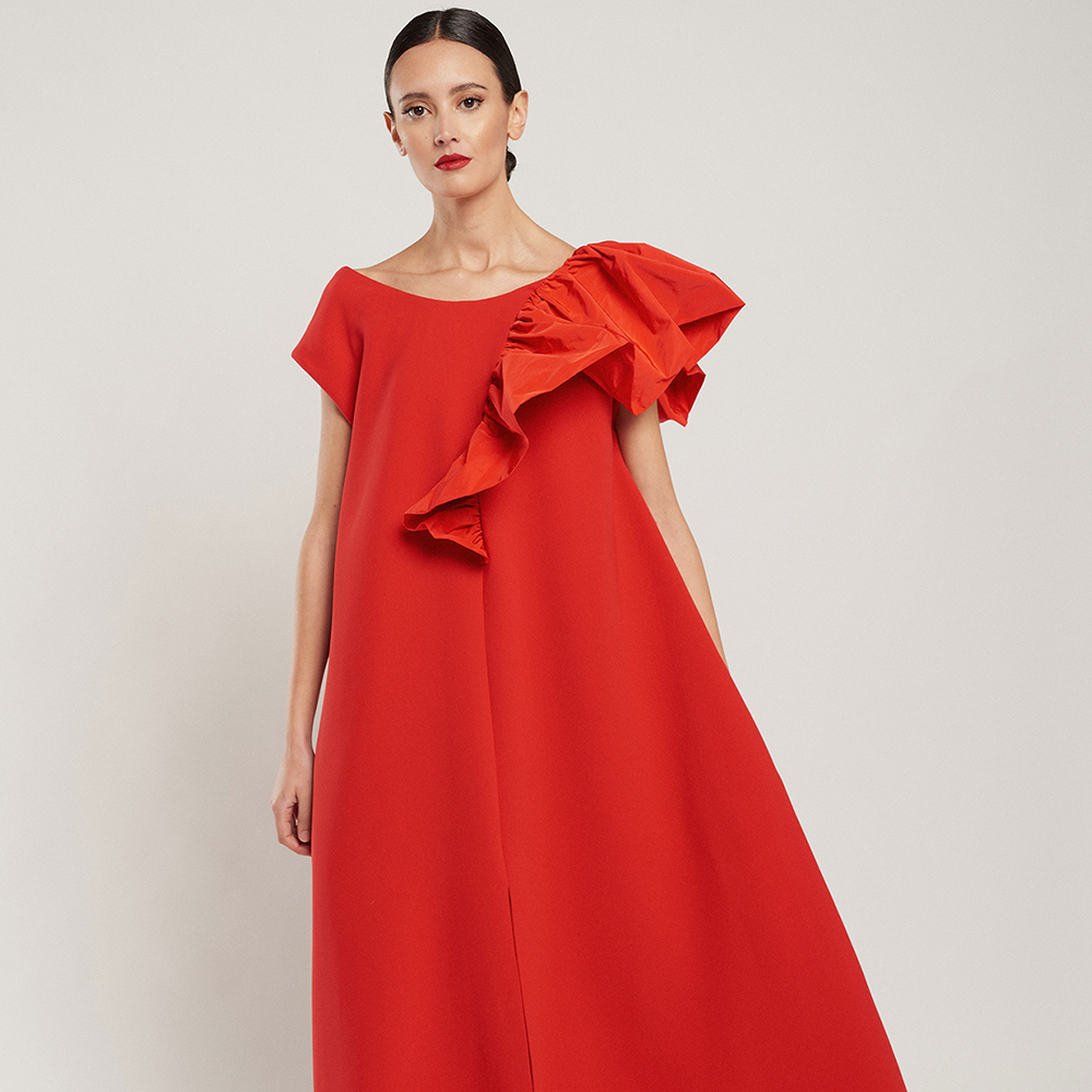 Shop the cape-style red Laura dress in crepe with a red technical fabric ruffle, side pockets and slit at the front. Shop now!