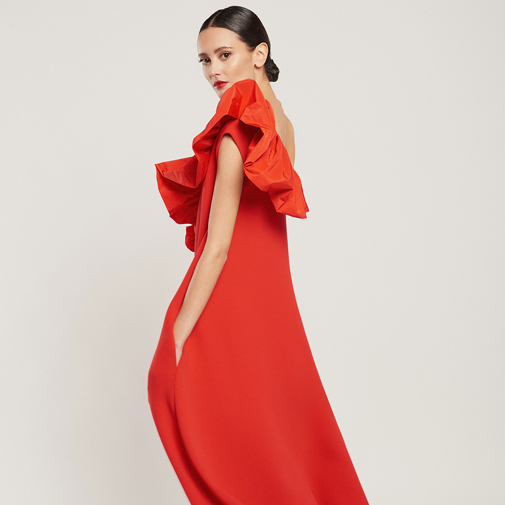 Shop the cape-style red Laura dress in crepe with a red technical fabric ruffle, side pockets and slit at the front. Shop now!