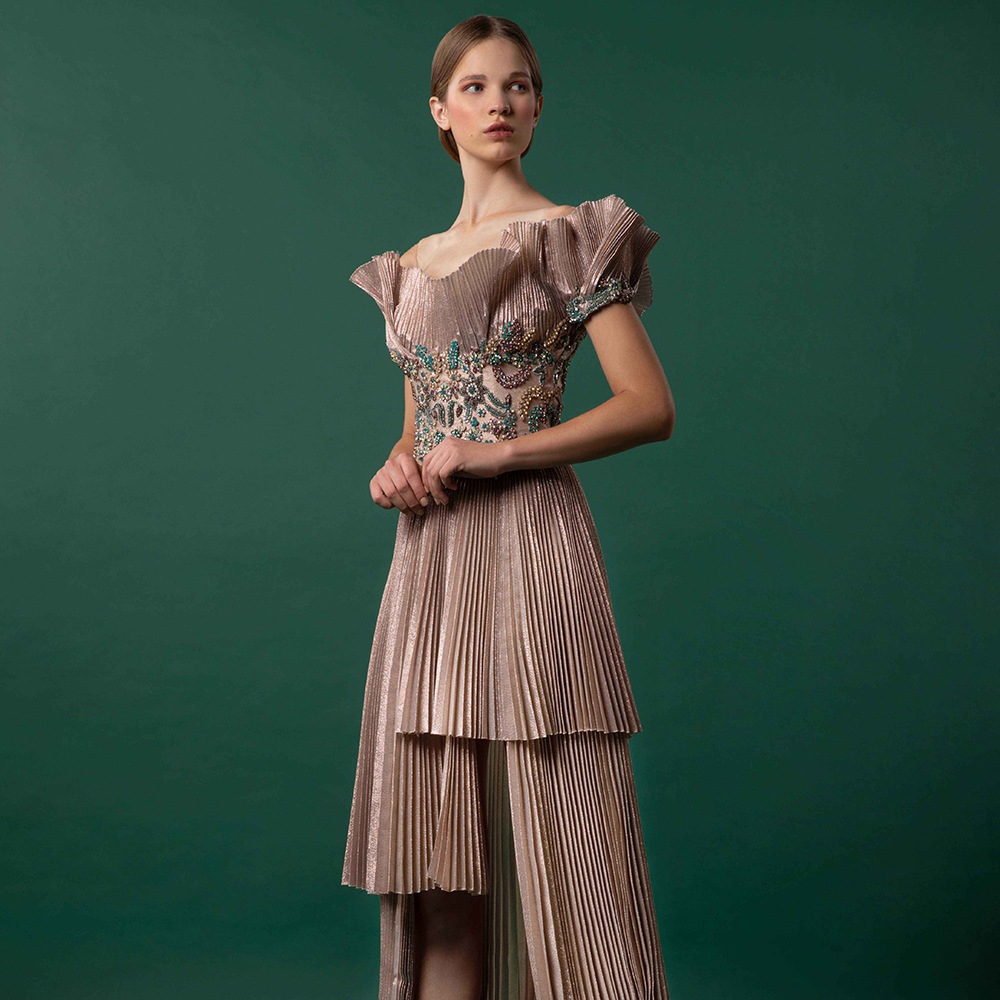 Off shoulder garment with bejeweled bodice over a structural high-low pleated gown.