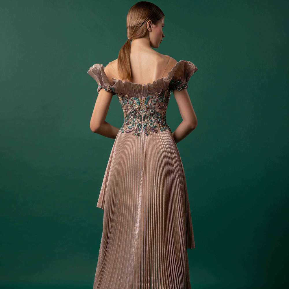 Off shoulder garment with bejeweled bodice over a structural high-low pleated gown.