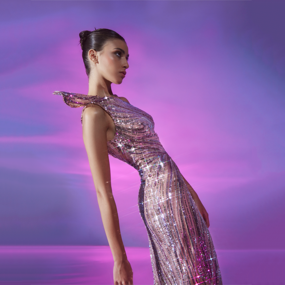 Long fitted tulle dress, fully embellished in Metallic Violet, featuring a structured one-shoulder detail and a side slit.