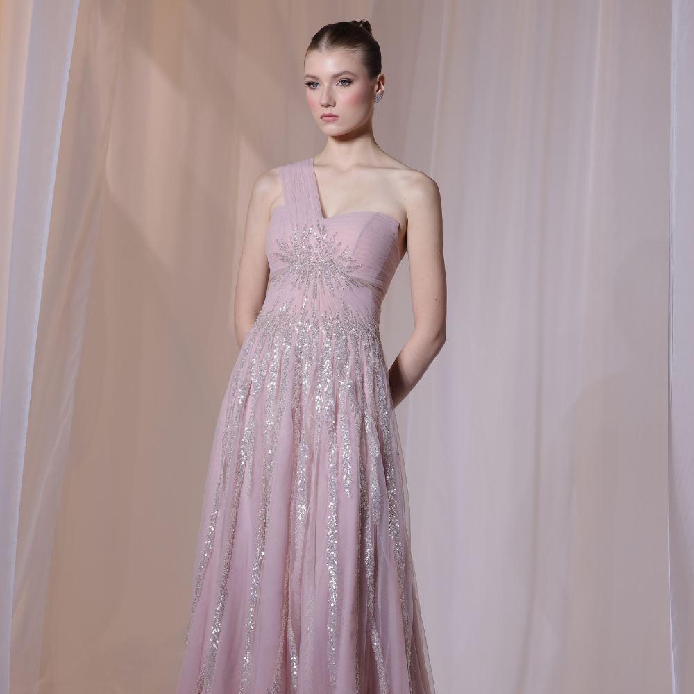 Shop online soft blush gown with one-shoulder silhouette, delicate shimmer detailing and flowing airy skirt, perfect for parties and special occasions.