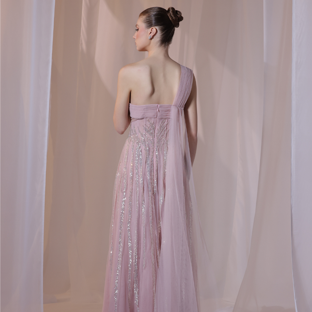 Shop online soft blush gown with one-shoulder silhouette, delicate shimmer detailing and flowing airy skirt, perfect for parties and special occasions.