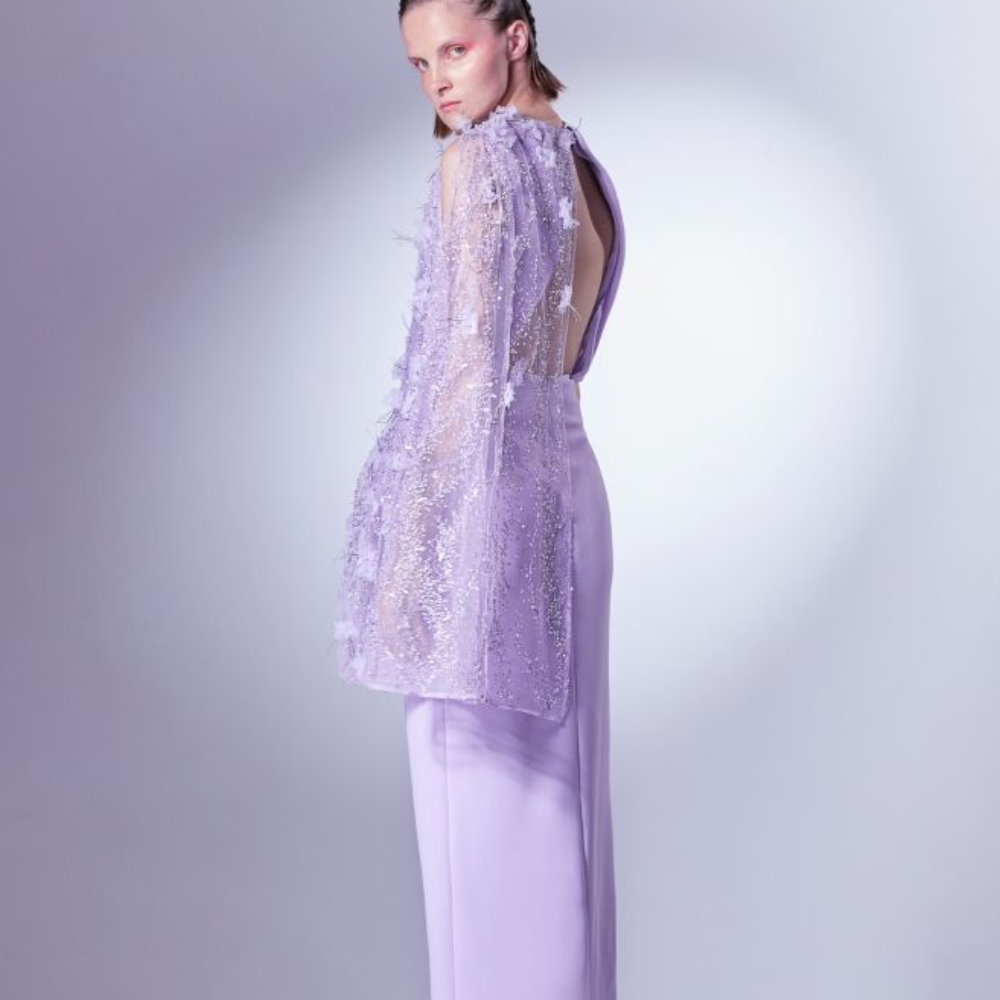 Rendered in Lilac, it features a short asymmetrical cape, constructed with beaded lace and metallic threads.