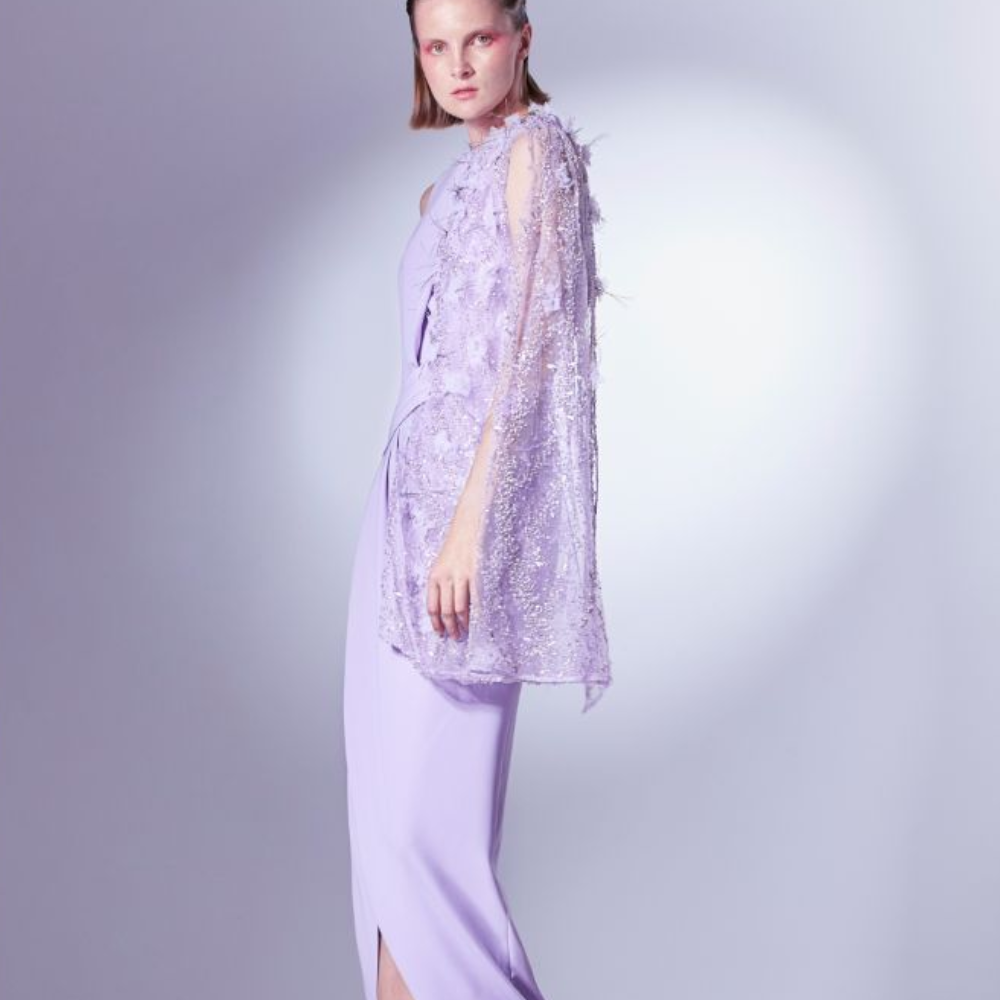 Rendered in Lilac, it features a short asymmetrical cape, constructed with beaded lace and metallic threads.