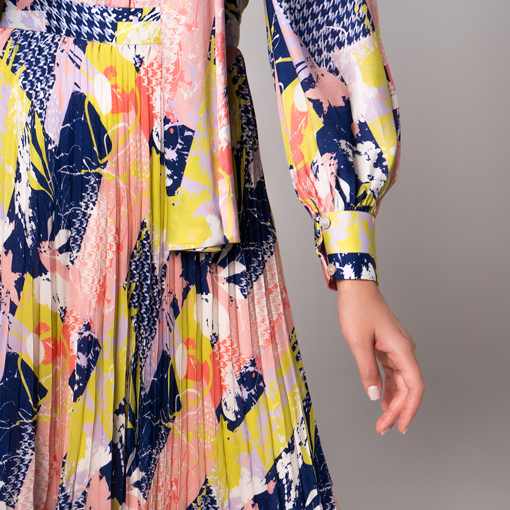 With hints of bold colors and patterns, this modest dress features a pleated flare, a feminine waist band with an elegant neckline.