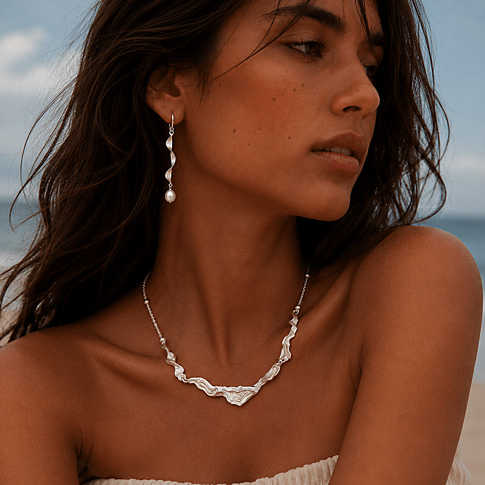 Discover the Moontide Sterling Silver Pearl Drop Earrings at The Luxe Maison, featuring sculptural, ribbon-like sterling silver designs finished with luminous pearls. Inspired by the gentle movement of ocean tides beneath moonlight, these elegant earrings combine fluid shapes with a soft, timeless glow. Perfect for special occasions or refined everyday styling, they bring graceful movement and understated sophistication to any look.