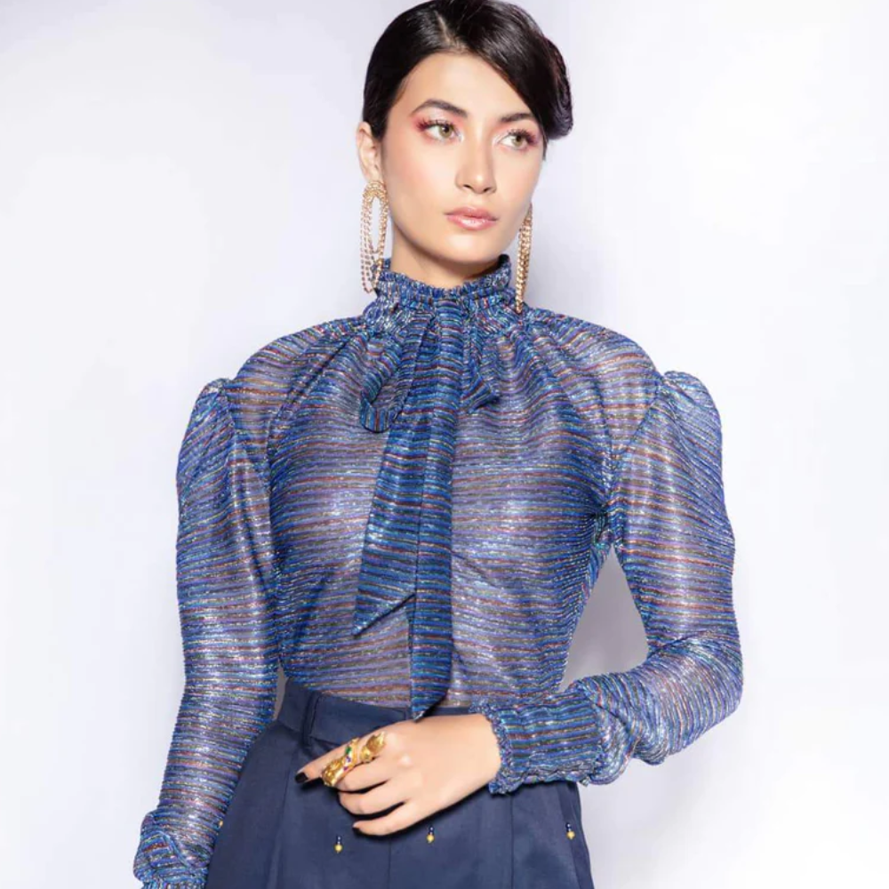 A long sleeve blouse featuring pleated metallic tricot jersey fabric ruffles at the collar and cuffs. It has a relaxed fit.