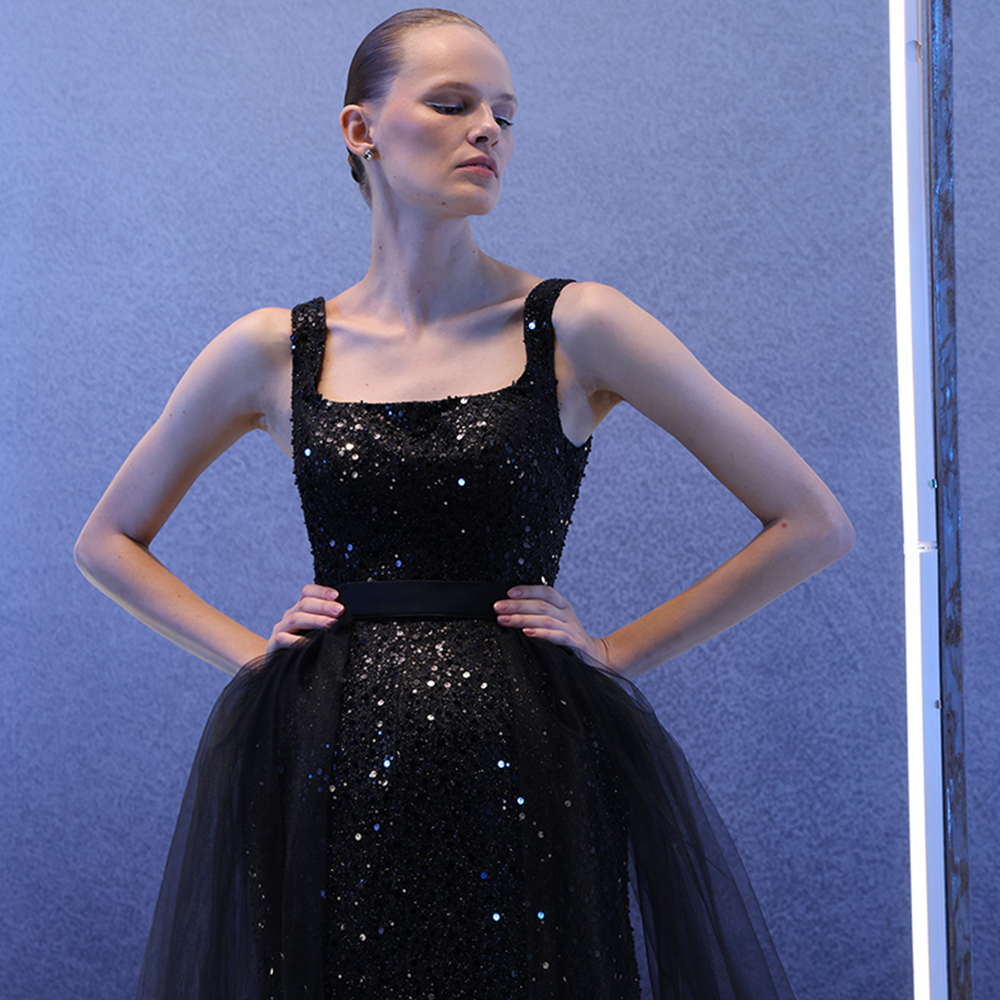 A timeless black dress with intricate embroidery and a square neckline, featuring a detachable black tulle overlay.