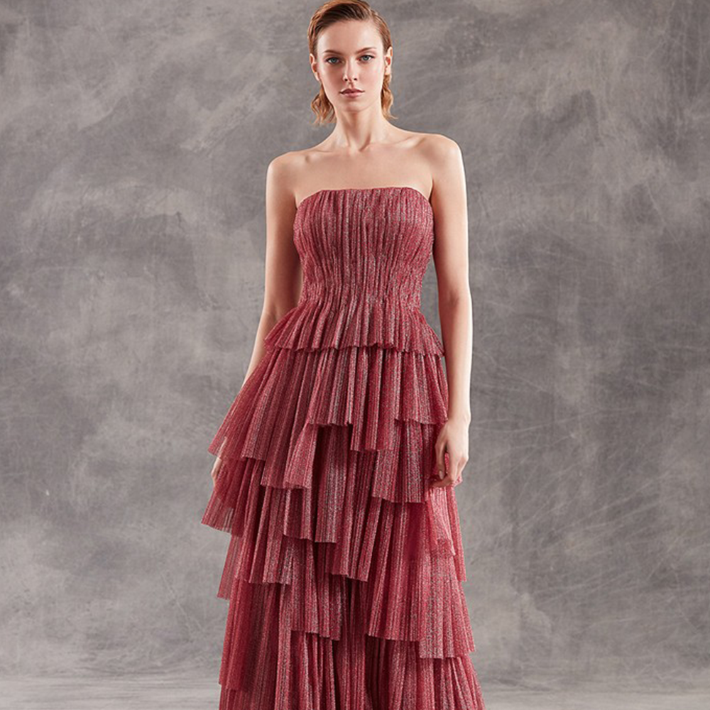 Strapless column gown in pleated metallic tulle with asymmetric flounced skirt.