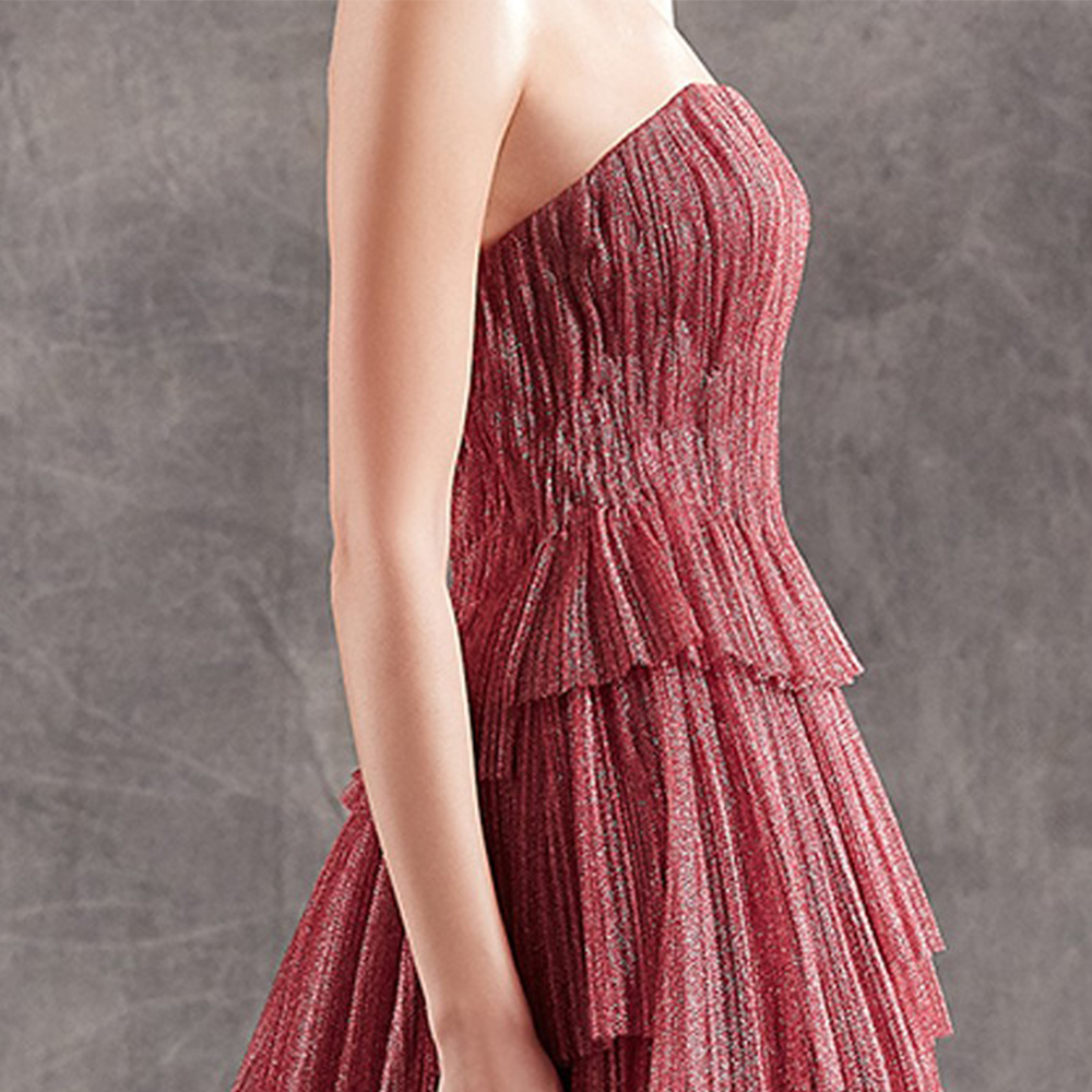 Strapless column gown in pleated metallic tulle with asymmetric flounced skirt.