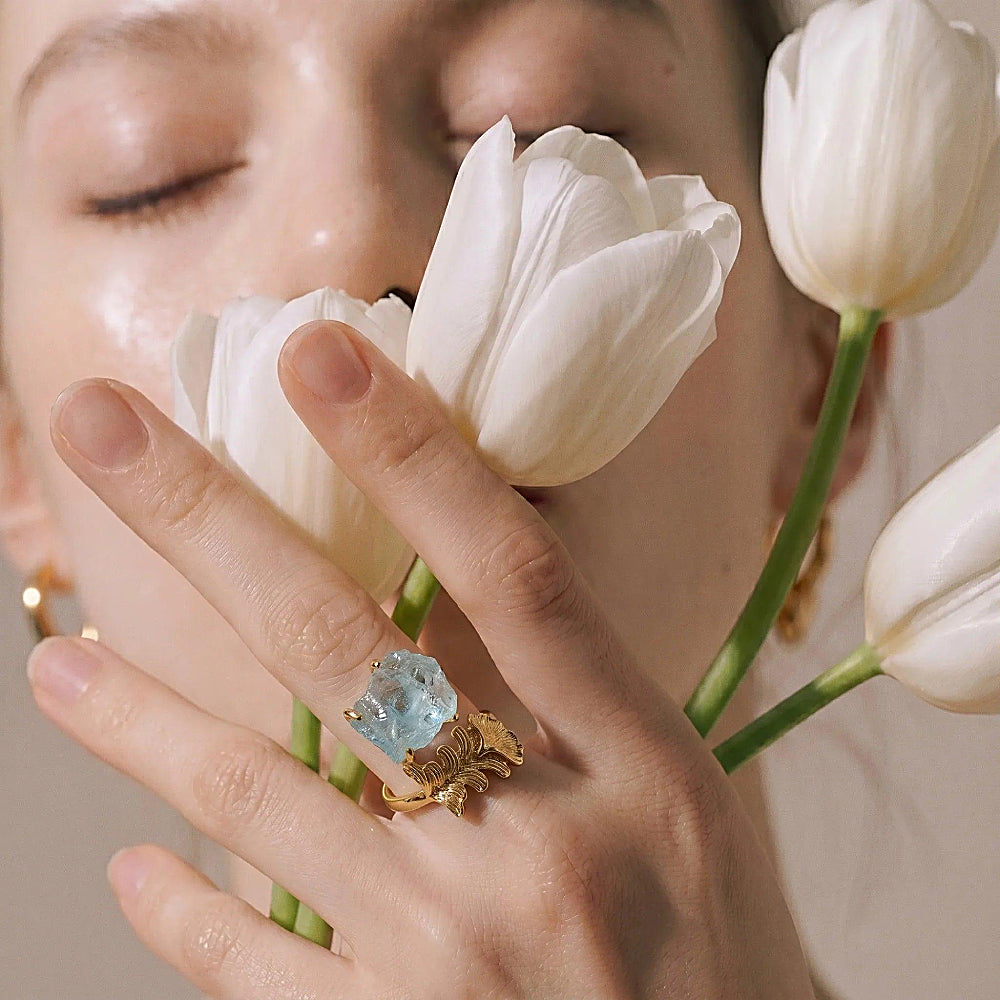 Discover the Nymph Aquamarine Gold Leaf Ring at The Luxe Maison, featuring a raw aquamarine gemstone held in golden prongs and framed by a sculptural gold leaf design. Inspired by mythical forest and water nymphs, this nature-inspired ring combines soft blue hues with organic elegance for a distinctive, enchanting look.