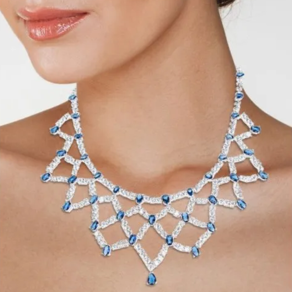 27 CTTW Oval Blue Sapphire and Round Cubic Zirconia draped bib necklace. Box clasp closure. Set in rhodium plated brass.
