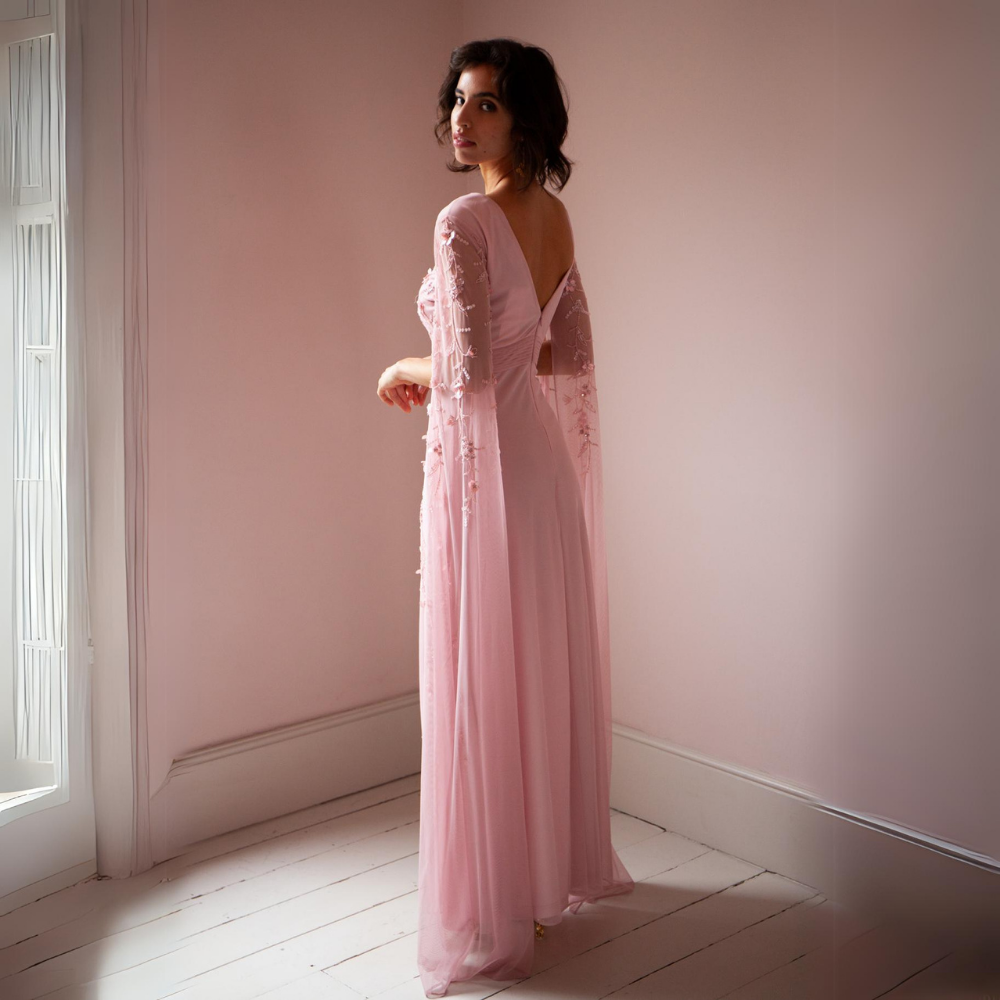 The Betsy Gown is a beautiful pale pink with mesh sleeves that cascade to the floor as well as pink floral sequins
