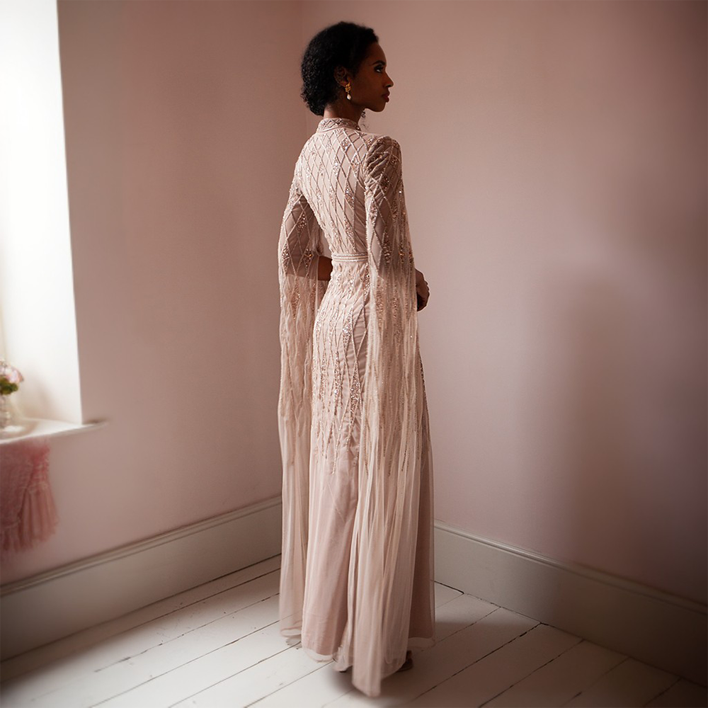 The Shantel Gown features a high neck and geometric beading throughout body and cape sleeves 