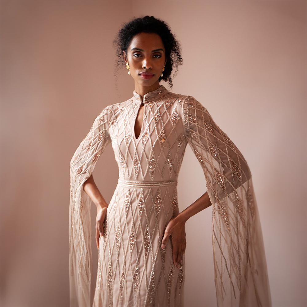 The Shantel Gown features a high neck and geometric beading throughout body and cape sleeves 