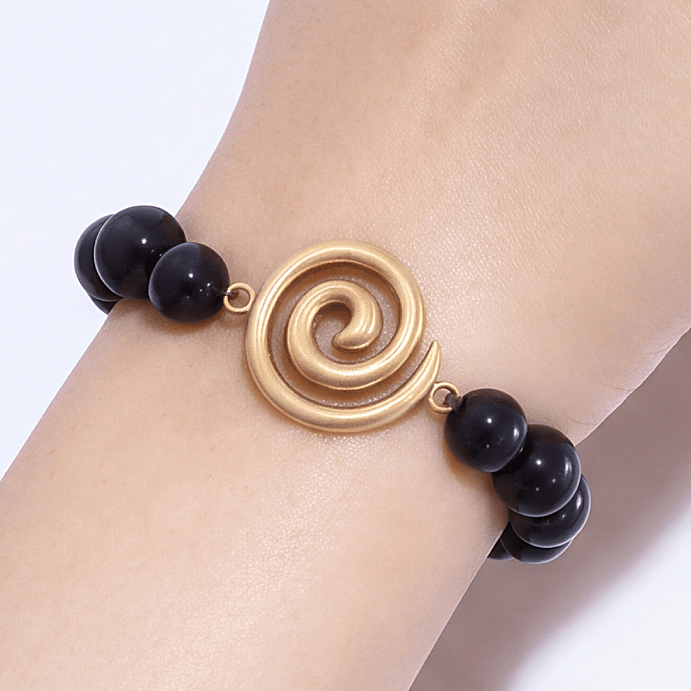 Discover the Vortex Shungite EMF Protection Bracelet at The Luxe Maison, featuring polished black shungite beads and a golden spiral charm.