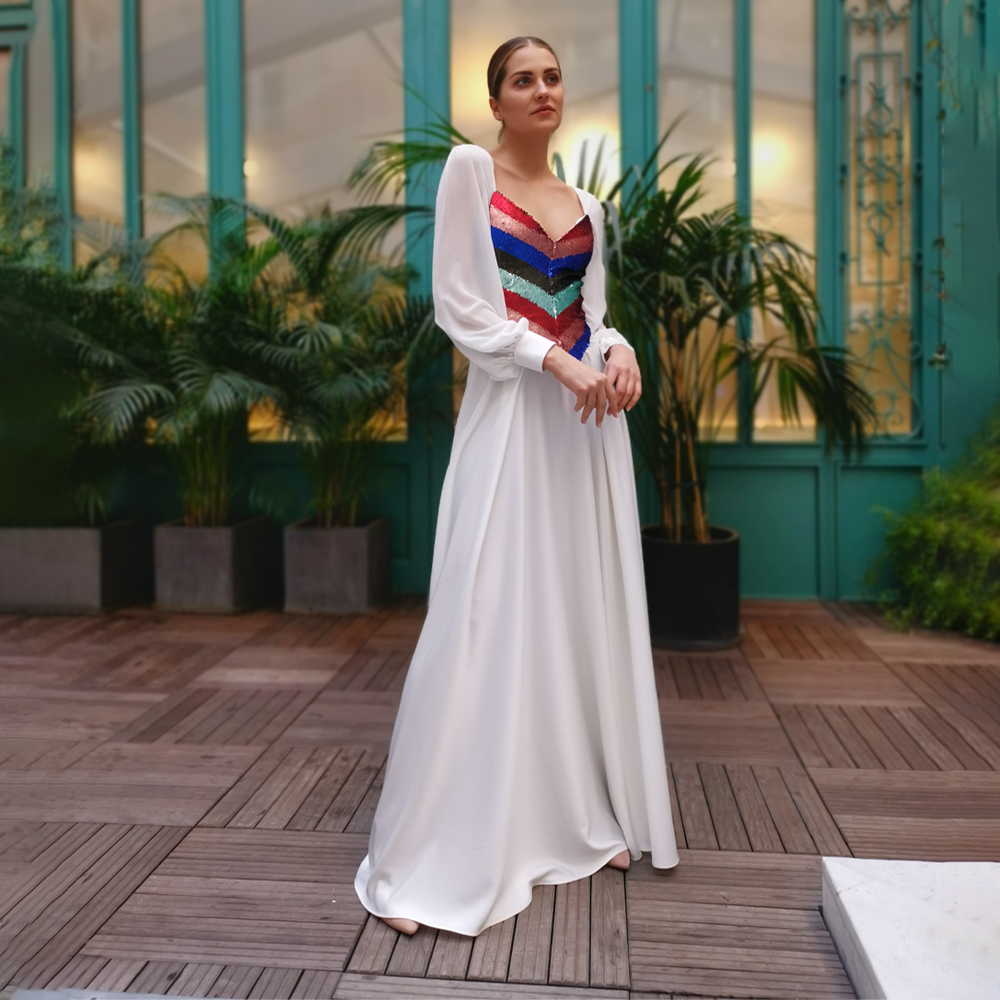 Long dress in white crepe with colored sequins and chiffon sleeves.